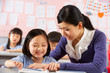 Photo: Teacher Helping Student Working At Desk In Chinese School Teacher Helping Student Working At Desk In Chinese School