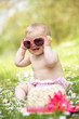 Baby Girl In Summer Dress Sitting In Field Wearing Sunglasses