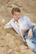 Young man in white shirt and blue jeans lied on the sand