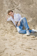 Young man in white shirt and blue jeans lied on the sand