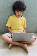 A boy sitting on the floor and working on  his laptop