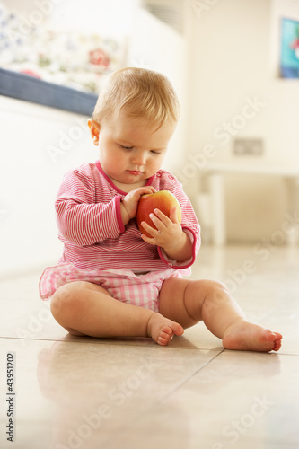 Foto: Baby Girl Sitting On Floor Looking At Apple Baby Girl Sitting On Floor Looking At Apple