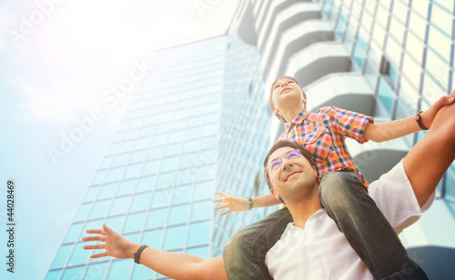 Photo: Portrait of smiling father giving his son piggyback ride outdoor Portrait of smiling father giving his son piggyback ride outdoor