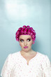 Young woman with curlers on pink hair over colored background