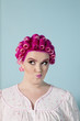Young woman making faces with pink hair and curlers over colored background