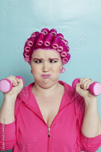 Photo: Young woman crossed eyes lifting dumbbell over colored background Young woman crossed eyes lifting dumbbell over colored background