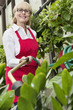 Portrait of a senior female gardener spraying pesticide on plants in botanical garden