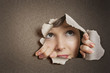 Young Caucasian woman peeking from ripped paper hole