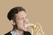 Portrait of a mid adult man winking while biting banana over colored background