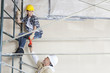 Foto: Male architect giving drill to female worker on scaffold at construction site Male architect giving drill to female worker on scaffold at construction site