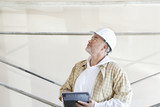 Photo: Mature male architect making a note in digital tablet while looking up at construction site Mature male architect making a note in digital tablet while looking up at construction site