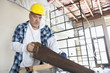 Serious male construction worker cutting wood with handsaw