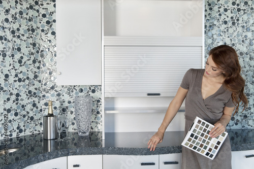 Photo: Beautiful young woman with color samples looking at contemporary kitchen cabinets Beautiful young woman with color samples looking at contemporary kitchen cabinets