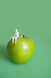Photo: Close-up of human figurine sitting on green apple over colored background Close-up of human figurine sitting on green apple over colored background