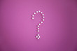 Close-up of push pins forming question mark over pink background