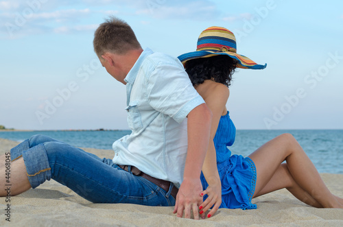 Photo: Couple sitting back to back on beach Couple sitting back to back on beach