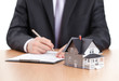 Foto: Businessman signs contract behind home architectural model Businessman signs contract behind home architectural model