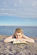 Portrait of a girl lying on the rock and reading book.