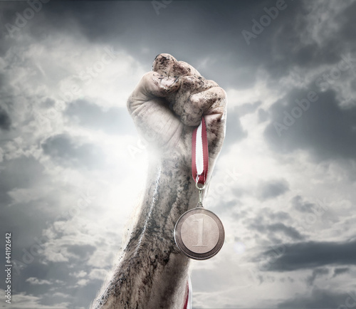 Photo: Male hand holding gold medal against the dramatic sky Male hand holding gold medal against the dramatic sky