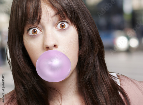 Photo: young girl with a pink bubble of chewing gum against a street ba young girl with a pink bubble of chewing gum against a street ba