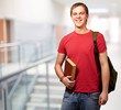portrait of young student holding book and carrying backpack at