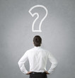Confused, young businessman looking at question mark