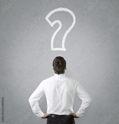 Photo: Confused, young businessman looking at question mark Confused, young businessman looking at question mark