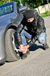 Man in mask punctures a car tyre. Revenge concept