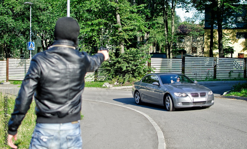 Photo: Man in mask pointing gun toward car. Robbery concept Man in mask pointing gun toward car. Robbery concept