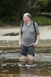 senior man is crossing a river with his backpack