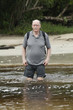senior man is crossing a river with his backpack