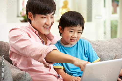 Photo: Chinese Father And Son Using Laptop Whilst Relaxing On Sofa Chinese Father And Son Using Laptop Whilst Relaxing On Sofa