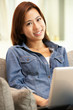 Young Chinese Woman Using Laptop Whilst Relaxing On Sofa At Home