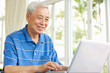 Senior Chinese Man Sitting At Desk Using Laptop At Home