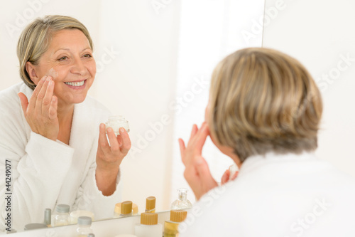 Photo: Mature woman apply cream looking bathroom mirror Mature woman apply cream looking bathroom mirror