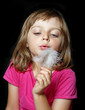 little girl blowing white feather on black background
