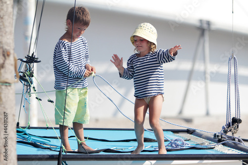Photo: two cute children in sailor t-shirt on sea catamaran / yacht two cute children in sailor t-shirt on sea catamaran / yacht