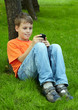 Smiling boy in orange t-shirt sits on grass under tree in park