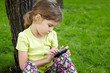 Girl sits leaning on tree in park and plays with cell phone