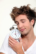 Sleepy man hugging his alarm clock