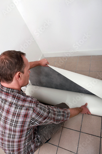 Photo: Crouching man unrolling flooring Crouching man unrolling flooring