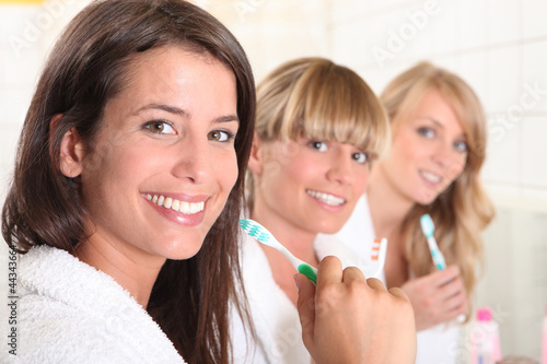 Photo: Three female house mates brushing their teeth Three female house mates brushing their teeth