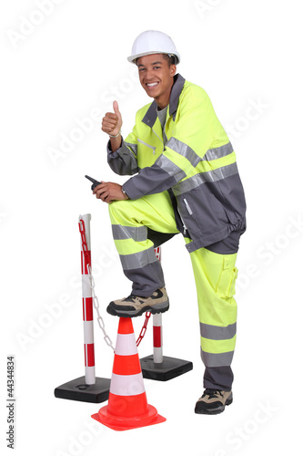 Photo: Man in high visibility overalls with a traffic cone and barrier Man in high visibility overalls with a traffic cone and barrier