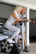 middle-aged blonde woman on exercise bike coached by husband
