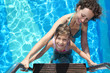 mother and daughter stand on stairs in pool with blue water