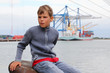 boy sits on stone and looks into distance at background of ship