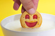 someon soaking a smiley-shaped cookie in milk