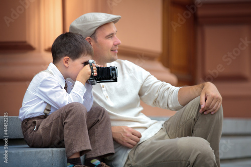 Photo: Father and little son holding retro camera in city Father and little son holding retro camera in city