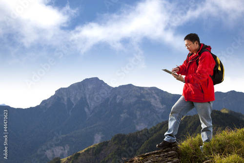 Photo: young man touching the tablet pc on the top of mountain young man touching the tablet pc on the top of mountain