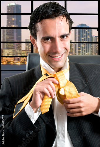 Photo: Businessman relaxed at office taking off his tie at night after Businessman relaxed at office taking off his tie at night after